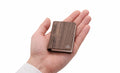 Gingko Palm Edition Smart Book Light in walnut finish held in the palm of a hand, showing compact size — closed position