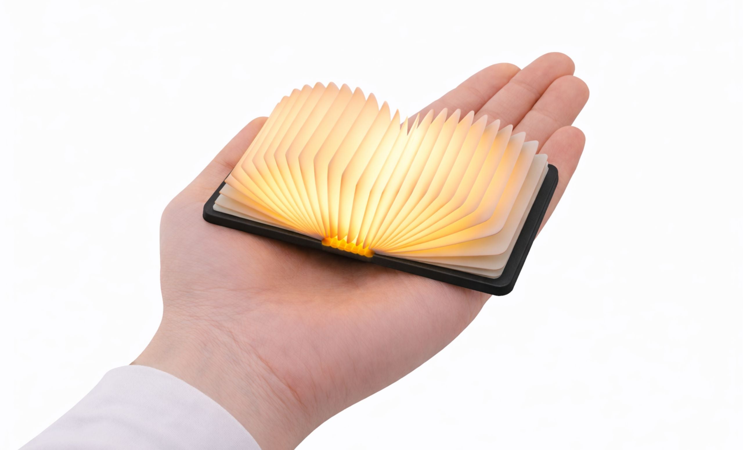 Gingko Palm Edition Smart Book Light in graphite/black open and glowing warm amber light in the palm of a hand — shows scale and glow