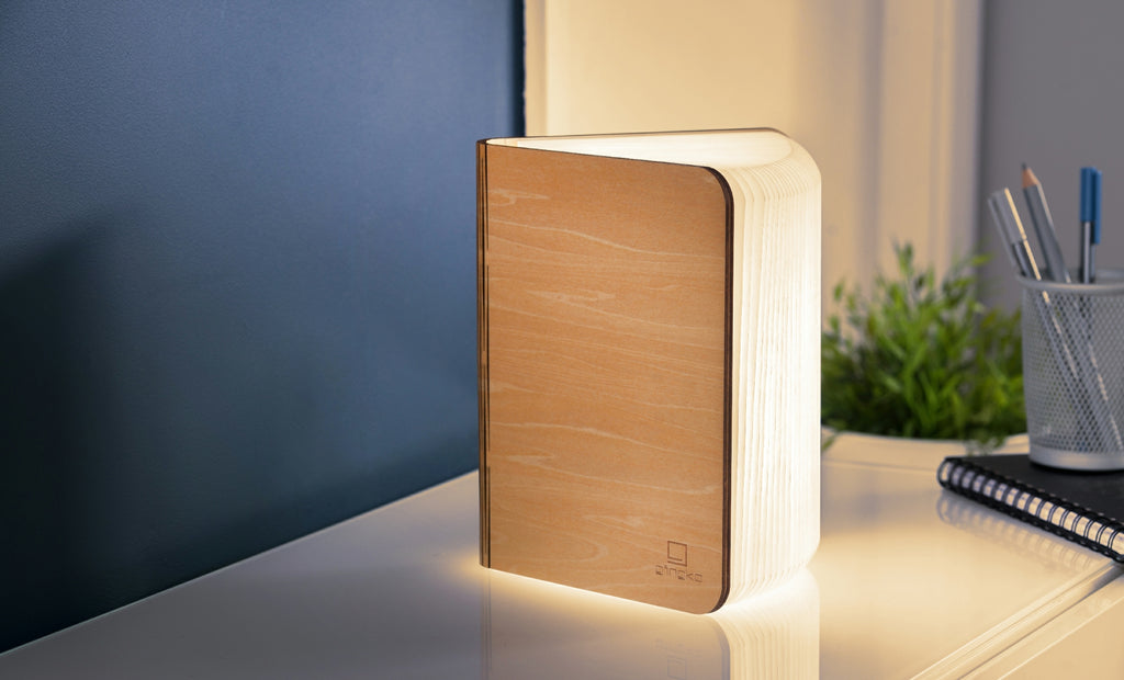 Gingko Smart Book Light open in walnut finish, warm LED glow on desk with pencils and plant